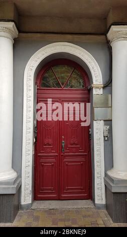 Élégante porte rouge de bâtiment historique dans la ville européenne Odessa d'Ukraine. Colonnes classiques blanches à côté de l'entrée de la maison antique Banque D'Images