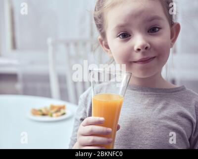 Une petite fille mignonne qui boit du jus à la maison. Banque D'Images