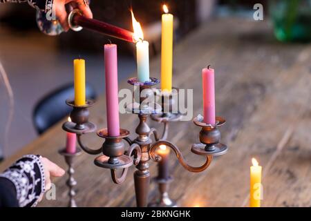 Une femme illuminant différentes bougies de couleur dans un porte-bougie en métal vintage pour créer une atmosphère agréable dans sa maison. Un style éclectique de vie avec un Banque D'Images