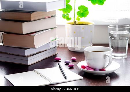 Une tasse de café blanche avec des bonbons multicolores se tient sur une table en bois, à côté d'une pile de livres et un carnet contre Banque D'Images