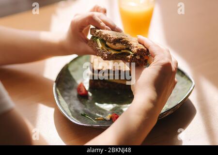 Femme tient dans les mains mordu sandwich. Pain grillé au seigle avec avocat. Jus d'orange frais nourriture végétarienne Banque D'Images