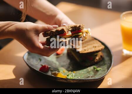 Femme tient dans les mains mordu sandwich. Pain grillé au seigle avec avocat. Jus d'orange frais nourriture végétarienne Banque D'Images