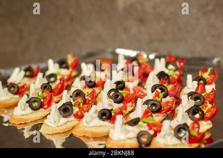 Canapés aux olives, fromage feta, tomates et herbes couchés en rangées sur un plateau métallique Banque D'Images