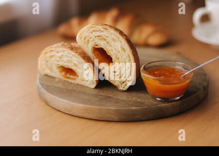 Deux moitiés de croissant fraîchement poêlé sur bois avec confiture d'abricot maison délirante. Fond de cappuccino Banque D'Images