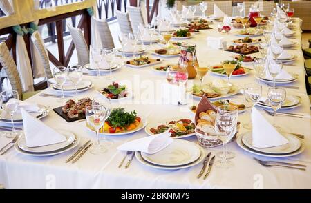 Table de réception pour un événement festif avec des assiettes blanches, des verres pour le vin et le jus de fruits et divers plats Banque D'Images