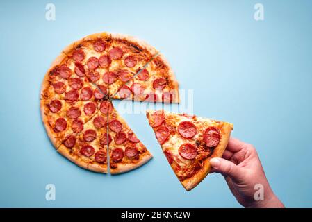 Vue ci-dessus avec la main de la femme prenant une tranche d'une pizza pepperoni. Délicieux salami maison pizza vue de dessus. Restauration rapide maison Banque D'Images