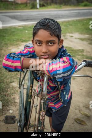 Portrait en gros plan d'un garçon indien incliné sur le guidon de vélo. Assam, Inde Banque D'Images