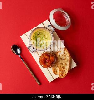 Beurre de citrouille dans un pot en verre avec bâtonnets de cannelle et sucre sur fond rouge, mise au point sélective. Banque D'Images