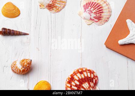 Bloc-notes ouvert marron entouré de coquillages sur table en bois blanc Banque D'Images