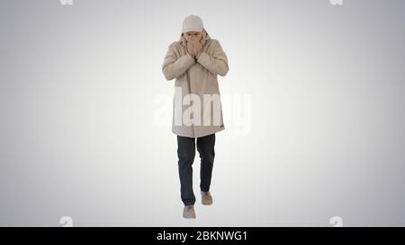 Homme en tenue d'hiver marchant et toussant sur fond dégradé. Banque D'Images