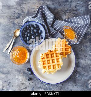 Gaufres belges traditionnelles faites maison avec myrtille, miel et confiture d'orange sur une assiette sur fond gris. Flat lay, vue de dessus, espace de copie. Banque D'Images