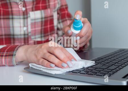 Femme mains pulvérisation antiseptique, nettoyage clavier d'ordinateur portable avec désinfectant humide sur table blanche. Désinfection, protection, prévention, travaux ménagers Banque D'Images