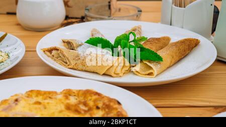 Crêpes sucrées avec fromage et confiture dans un plat blanc. Crêpe avec pommes et cannelle pour le petit déjeuner dans un café. Délicieuses crêpes sucrées avec du su en poudre Banque D'Images