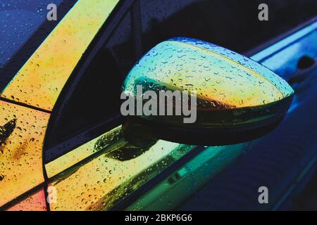 Voiture holographique couleur caméléon après la pluie. Rétroviseur latéral avec gouttes d'eau. Emballage de voiture. Jour de pluie. Banque D'Images