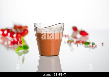 Soupe froide traditionnelle de tomates espagnoles dans le verre en plastique sur fond blanc avec décoration Banque D'Images