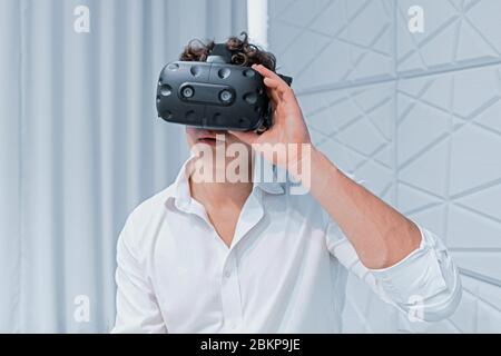 Le jeune homme excité a pris des lunettes VR. Première réalité virtuelle expérimentée. Jouer à des jeux en ligne avec social distance. Image avec bruit ou grains Banque D'Images