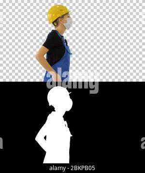 Femme travailleur de la construction dans les salopettes et dans le masque médical de marche, Alpha Channel Banque D'Images