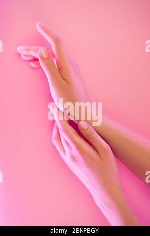 Les mains d'une femme avec une manucure parfaite dans une lumière néon tendance sur fond rose. Concept de beauté. Banque D'Images