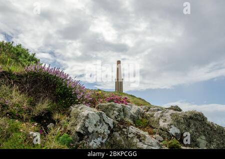 Le monument Heinz au cap Cornwall vu d'en bas avec des rochers couverts de bruyère et de lichen au premier plan sous un ciel sombre Banque D'Images