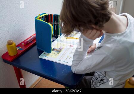 Erstklaessler (7 ans) est assis à une table à la maison et fait des tâches allemandes dans son livret "Alphabet livret - police de base", le 4 mai 2020 à Muelheim an der Ruhr/Allemagne. € | utilisation dans le monde entier Banque D'Images