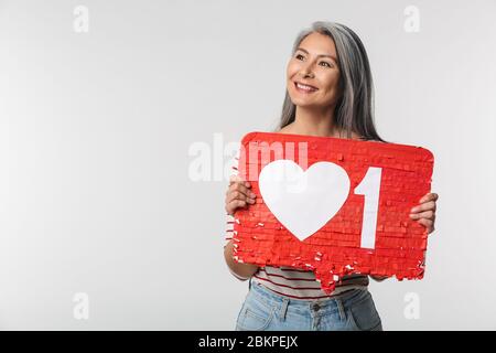 Image d'une femme adulte mûre heureuse avec de longs cheveux blancs tenant le symbole du cœur sur l'étiquette isolée sur fond gris Banque D'Images