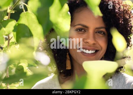 Jeune femme souriante debout dehors encadrée par des feuilles vertes Banque D'Images