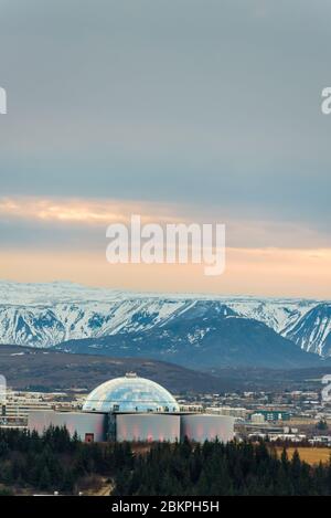 Perlan, bâtiment phare de Reykjavík, la capitale de l'Islande avec des montagnes enneigées en arrière-plan, vu de la tour de l'église Hallgrimskirkja. Banque D'Images