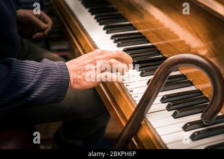 Main d'un homme âgé au piano et bâton de marche ayant une leçon de piano. Concept: Activité de vieillesse, stimulation, apprentissage, jamais trop vieux, maintien jeune. Banque D'Images