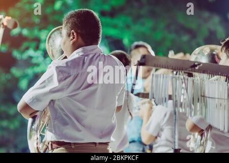 Male student with friends souffler l'euphonium avec le groupe pour la performance sur scène de nuit. Banque D'Images