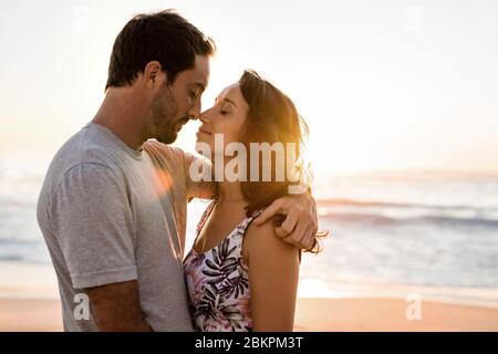 Un jeune couple affectueux s'embrassant sur une plage au coucher du soleil Banque D'Images