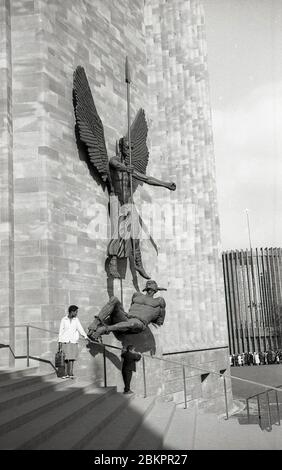 1962, photo historique montrant une dame et son fils debout devant la cathédrale nouvellement construite à Coventry, Angleterre. La sculpture sur le mur, de Jacob Epstein, dénote la victoire de Saint Michel sur le diable. Bombardé pendant la Seconde Guerre mondiale, en mai 1962, un nouveau bâtiment « moderne » a été ouvert dans la ville sur le site des ruines de l'ancienne cathédrale. Banque D'Images