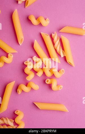 Variété de pâtes de blé doré non cuites sur fond rose minimal, vue du dessus Banque D'Images
