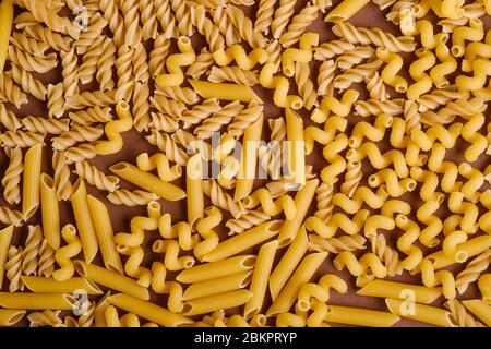 Variété de pâtes de blé doré non cuites sur fond brun minimal, vue du dessus Banque D'Images