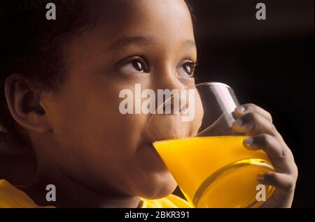 Bébé Africain américain mignon attrayante fille de quatre ans buvant un verre de jus d'orange dans sa cuisine Banque D'Images