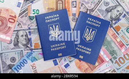 Deux passeports biométriques ukrainiens se trouvent sur un fond de devises provenant de différents pays du monde, euros, dollars, hryvnias, forints. Le Banque D'Images