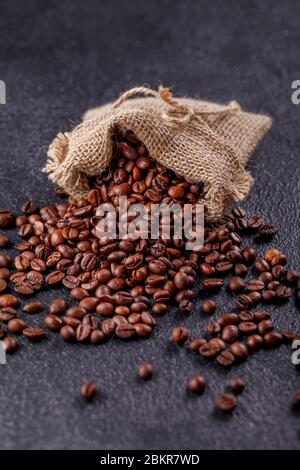 Grains de café aromatiques rôtis saupoudrés d'un sac en toile sur une surface sombre. Le concept de la tradition du café du matin. Vue latérale supérieure Banque D'Images