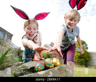 Un frère et une sœur, vêtu de peinture faciale et d'oreilles de lapin maison, participent à une chasse aux œufs le dimanche de Pâques dans leur jardin. Banque D'Images