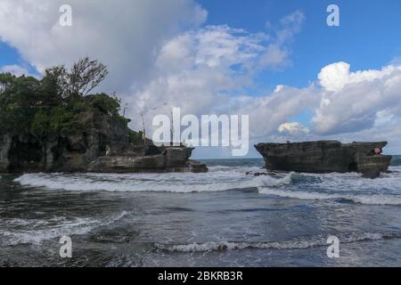 Des vagues se brisent sur une falaise au sommet de laquelle se trouve le temple hindou de Tanah Lot. Temple construit sur un rocher dans la mer au large de la côte de l'île de Bali, Indones Banque D'Images