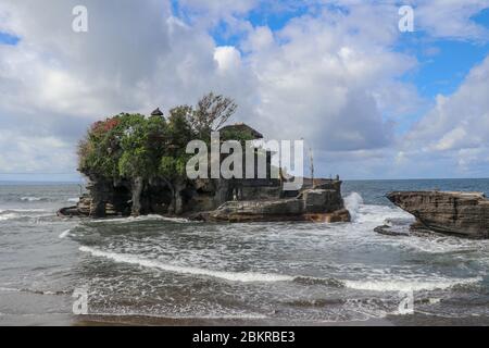 Des vagues se brisent sur une falaise au sommet de laquelle se trouve le temple hindou de Tanah Lot. Temple construit sur un rocher dans la mer au large de la côte de l'île de Bali, Indones Banque D'Images