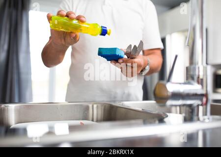 Homme de premier plan lavant des plats dans sa cuisine moderne et lumineuse Banque D'Images