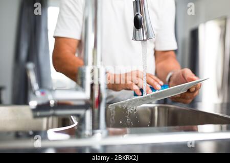 Homme de premier plan lavant des plats dans sa cuisine moderne et lumineuse Banque D'Images