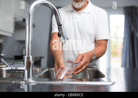 Homme de premier plan lavant des plats dans sa cuisine moderne et lumineuse Banque D'Images