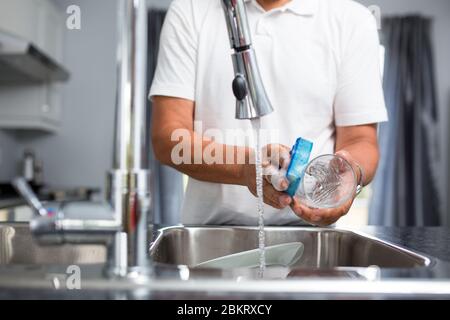 Homme senior lavant des plats dans sa cuisine moderne et lumineuse (DOF peu profond ; image colorée) Banque D'Images