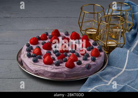 Cheesecake maison avec baies. Cheesecake aux fraises, bleuets et framboises sur table en bois gris décorée de bougies et de assiettes. Banque D'Images