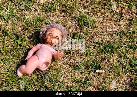 Une vieille poupée détruite avec les yeux fermés, une jambe manquante se trouve sale dans l'herbe Banque D'Images