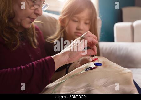 Une grand-mère aimante enseigne à sa petite-fille comment coudre des boutons Banque D'Images