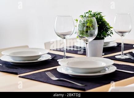 Fermez les nouvelles assiettes en porcelaine blanche sur les sets de table violets et les verres à vin vides prêts pour le dîner. Les réglages de la table attendent les clients à la maison Banque D'Images