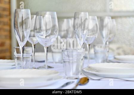 Gros plan sur une nouvelle variété de verres et de plaques en porcelaine servis sur une nappe blanche, pas de personnes. Les réglages de table attendent les clients à la maison ou au restaurant Banque D'Images