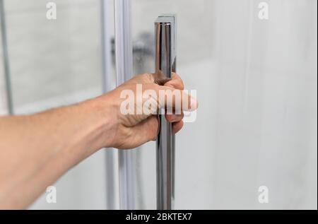 Main mâle ouvre la porte de douche dans une salle de bains moderne. Banque D'Images