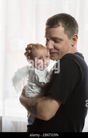 Un jeune homme tient doucement un bébé avec des ailes d'ange dans ses bras. Père et fille heureux Banque D'Images